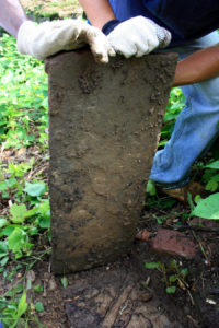 Image of an old headstone covered in dirt being held by gloved hands.
